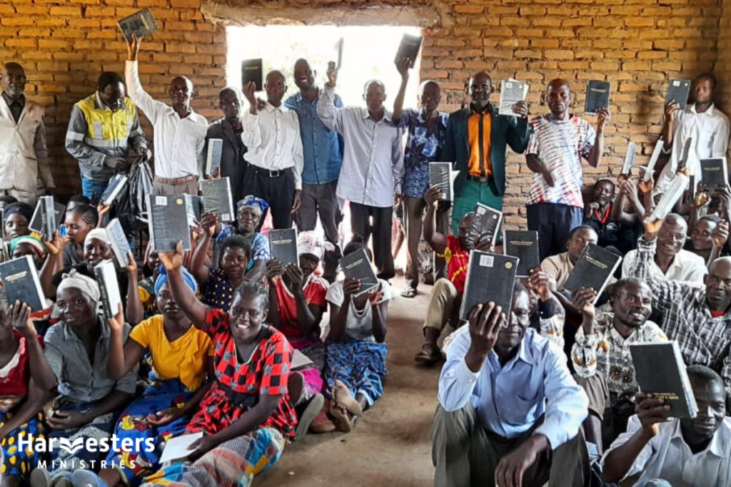 Congregation holding up Bibles in church. Harvesters Ministries